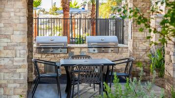 An outdoor patio with two barbecue grills, a table, and four chairs.