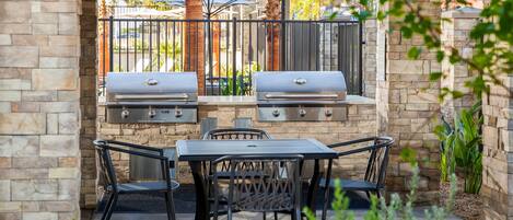 An outdoor patio with two barbecue grills, a table, and four chairs.