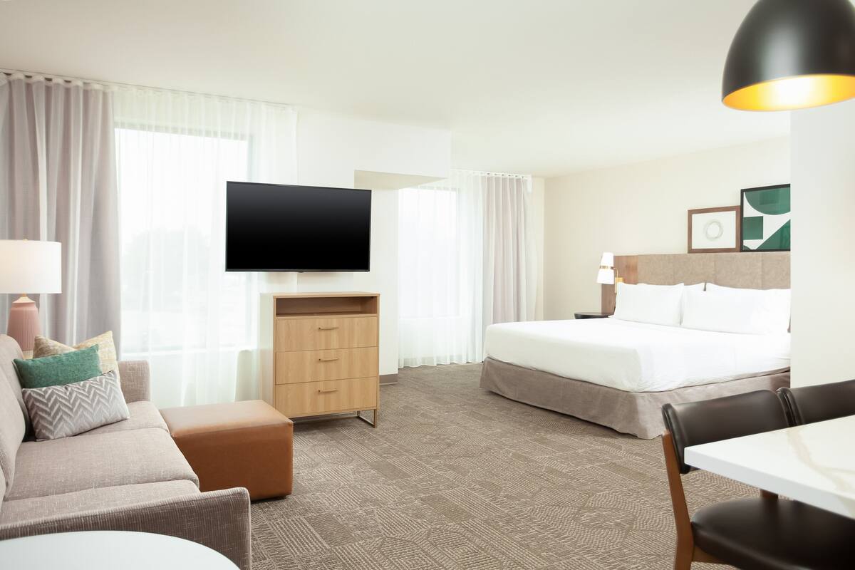 A hotel room with a bed, a TV, a desk, a chair, and a sofa.