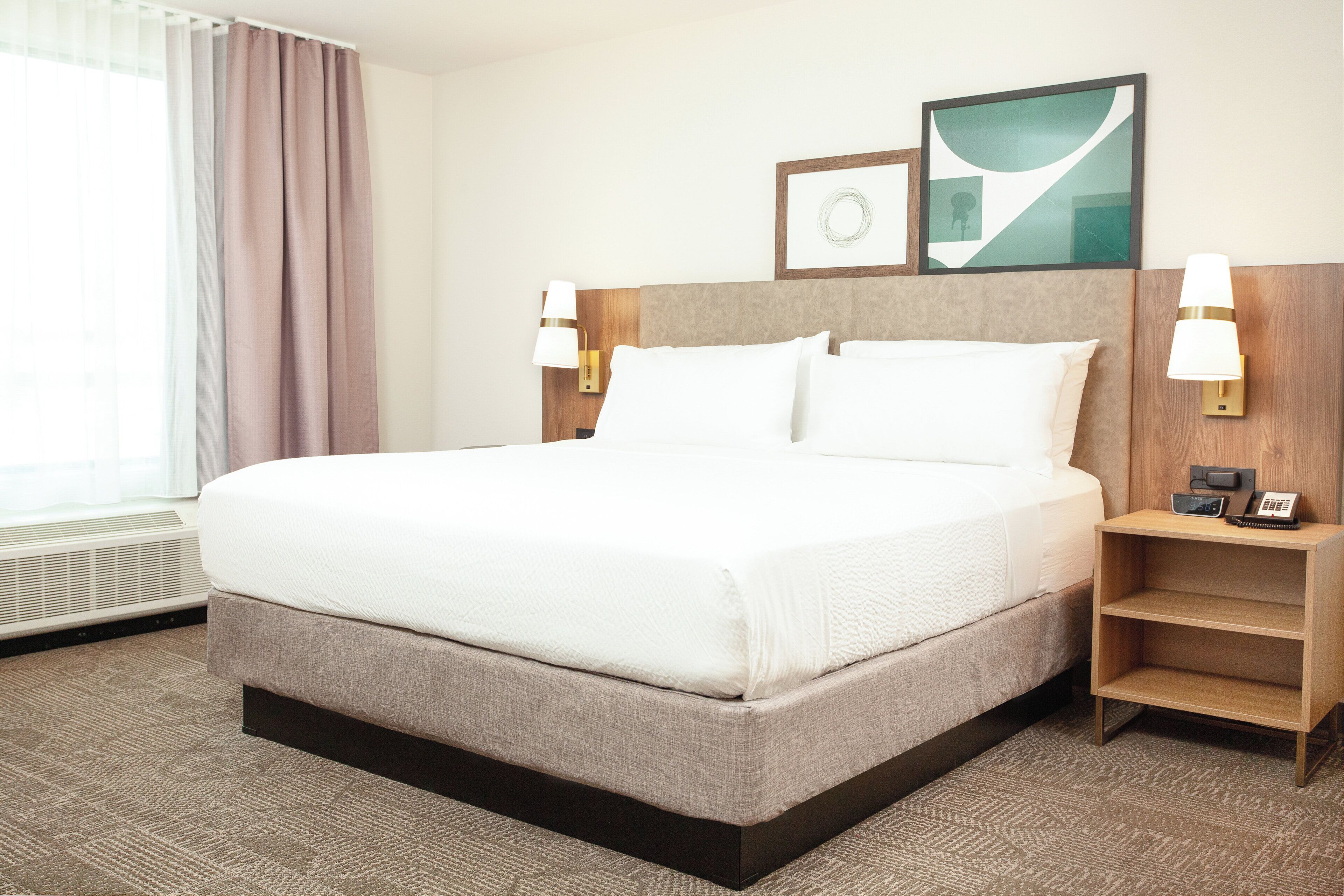A hotel room with a large bed, two bedside tables, a wall-mounted lamp, a clock, and a framed picture.