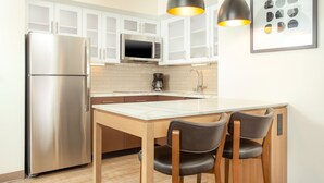 Una cocina moderna con armarios blancos, electrodomésticos de acero inoxidable, una mesa de madera y dos taburetes de bar.