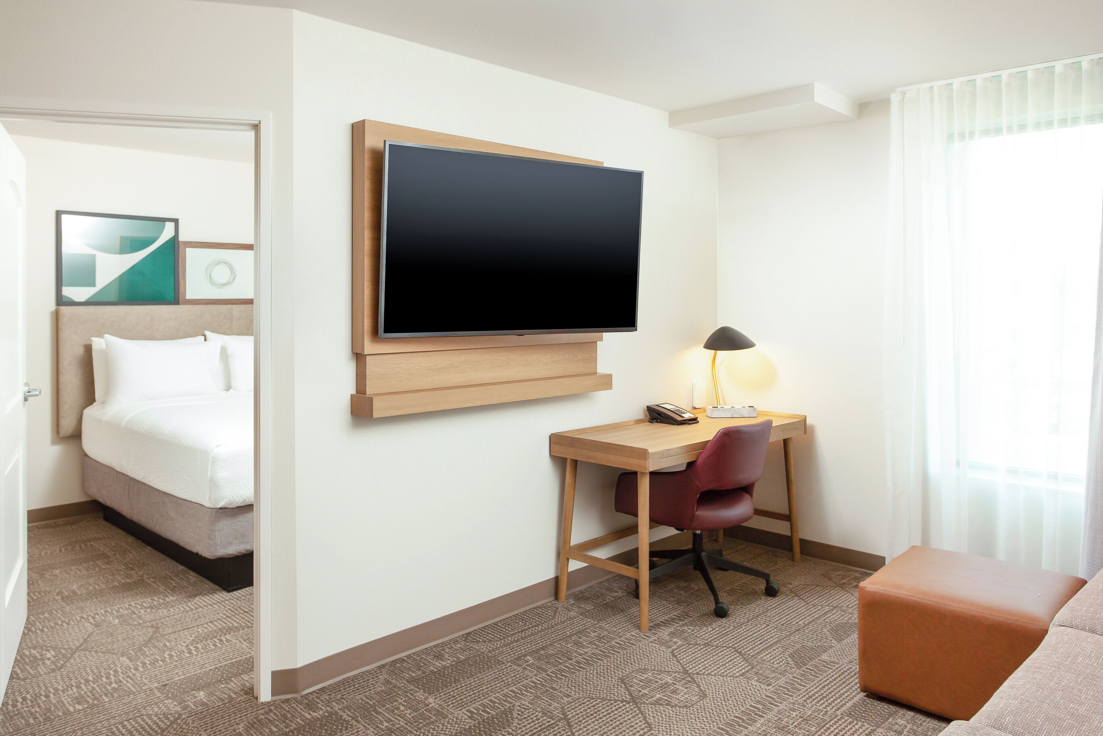 Una habitación de hotel con cama, escritorio, silla, televisor y lámpara.