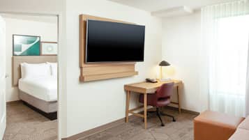 Una habitación de hotel con cama, escritorio, silla, televisor y lámpara.