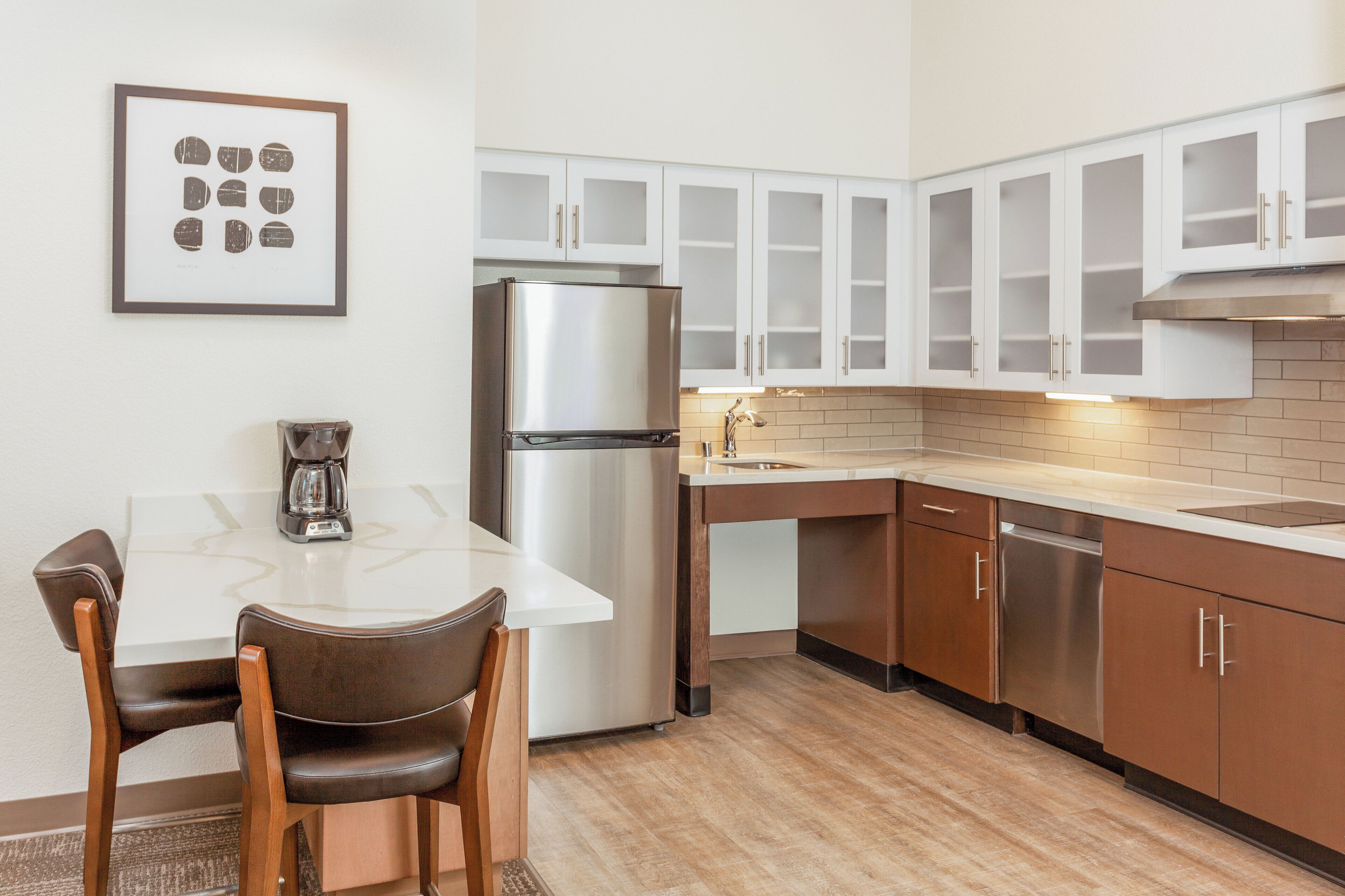 Una cocina moderna con armarios blancos, un refrigerador de acero inoxidable, una cafetera y un comedor con mesa y sillas.