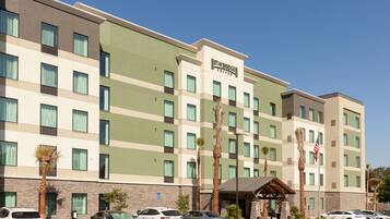 A multi-story hotel with a green and beige facade, multiple windows, and a parking lot with several cars.