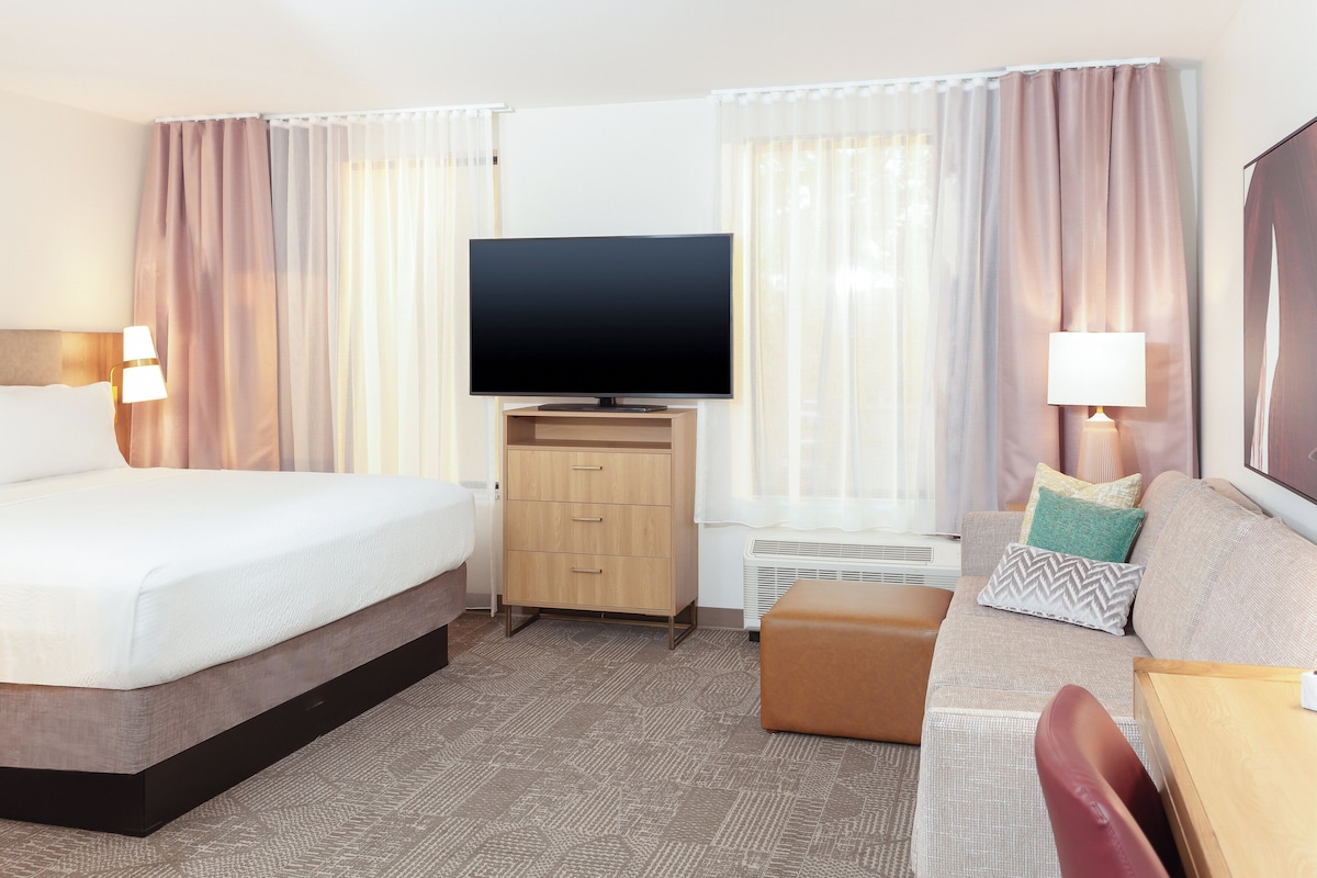 Una habitación de hotel con cama, televisión, sofá, escritorio y una silla.