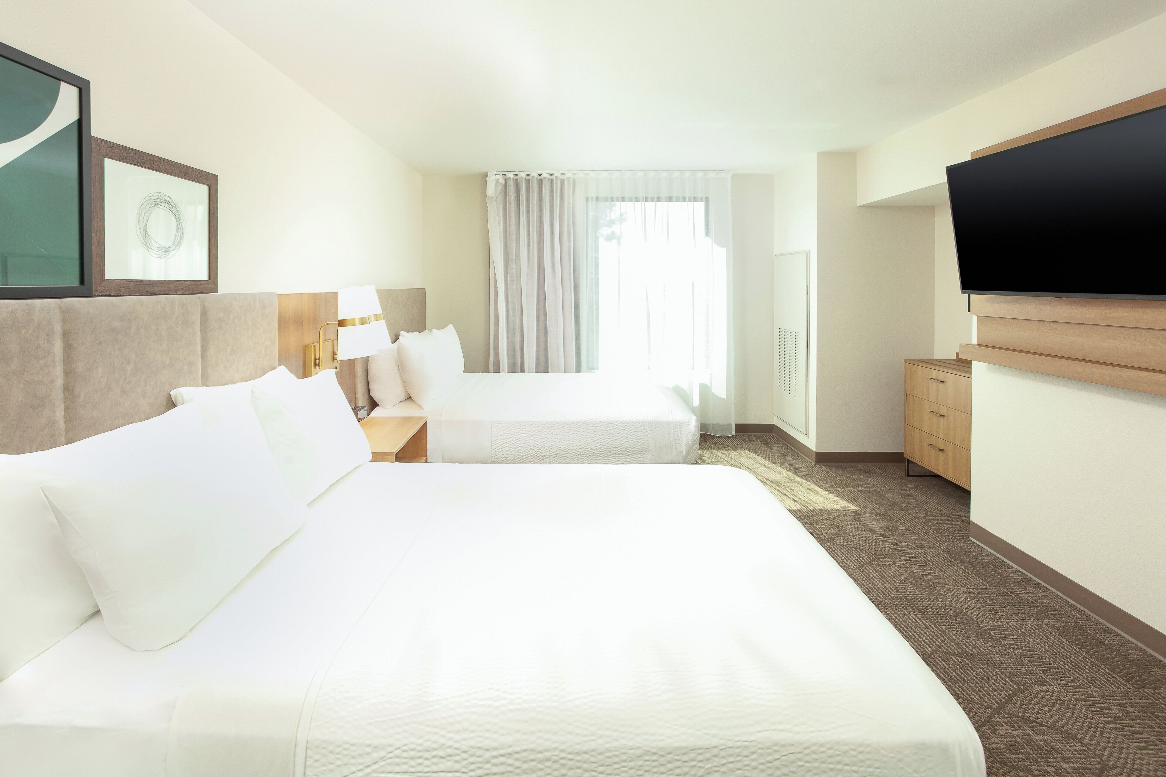 A hotel room with two beds, a TV, a desk, and a window with curtains.