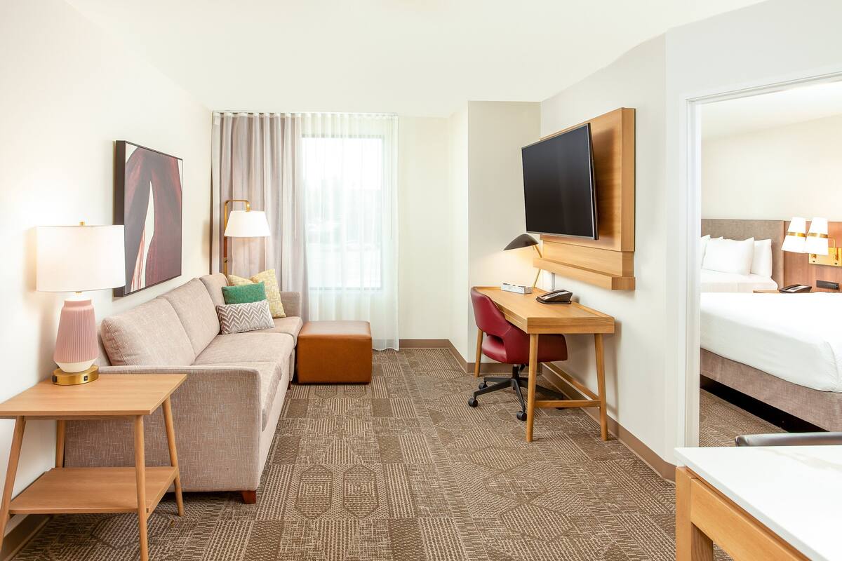 A hotel room with a sofa, a desk, a television, a bed, and a window with curtains.