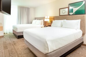 A hotel room with two beds, a flat-screen TV, a wall-mounted lamp, and a framed picture.