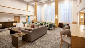 Un vestíbulo de hotel con un sofá, sillas, una mesa y piso alfombrado.