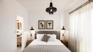 Une chambre à coucher bien rangée, avec un grand lit, deux tables de chevet, un luminaire suspendu et deux tableaux encadrés au mur.