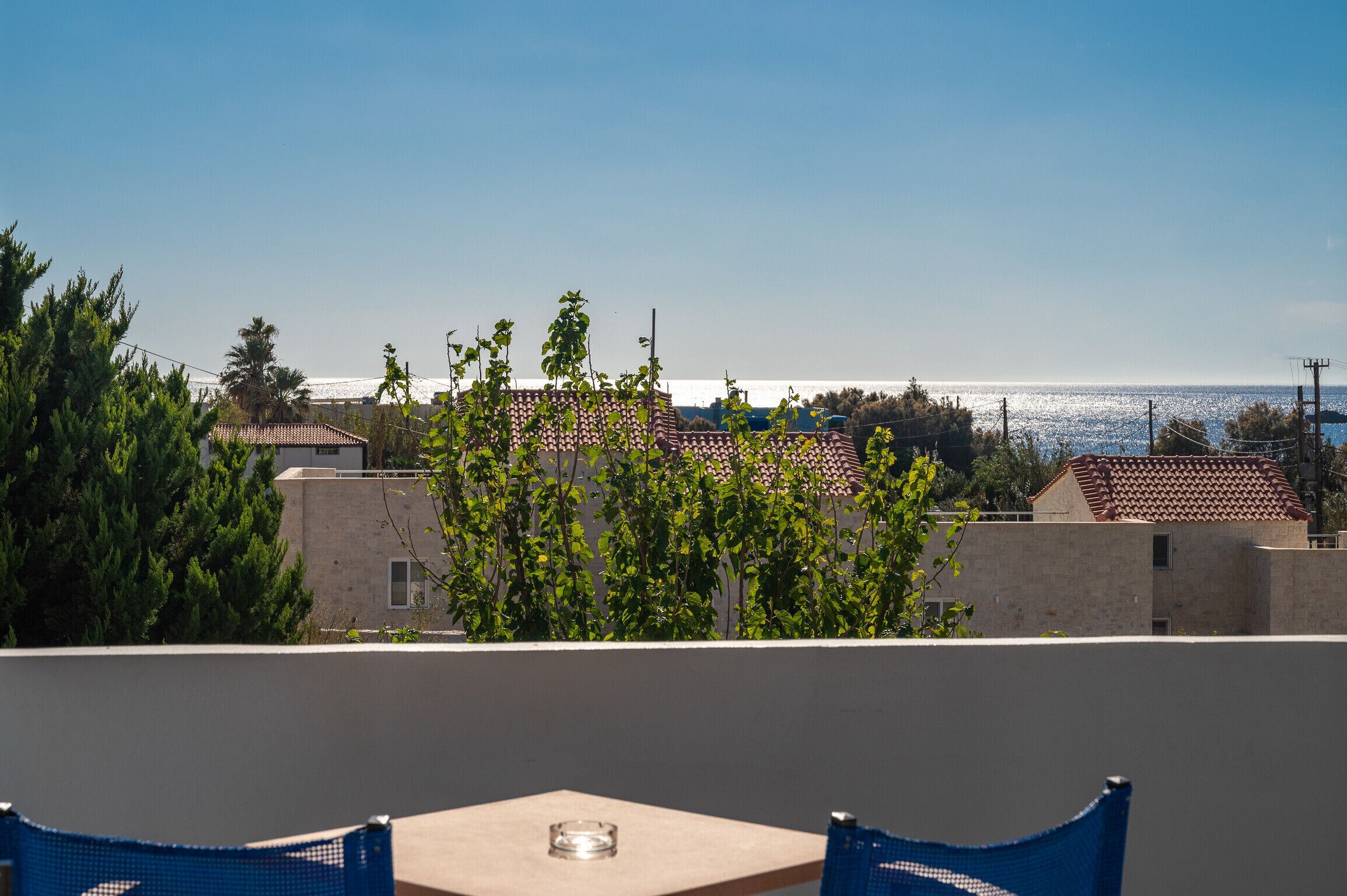 Una terraza con mesa y sillas, con vista a una zona costera con edificios y árboles.