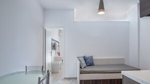 Ein modernes, minimalistisches Zimmer mit einem Glastisch, einer eingebauten Bank mit Kissen und einer Pendelleuchte.