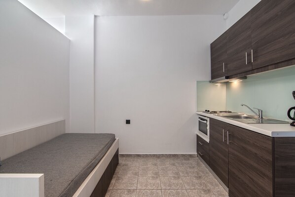A compact kitchen with dark wooden cabinets, a white countertop, and a built-in oven.