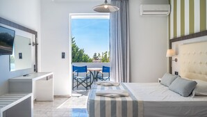Une chambre d’hôtel moderne, équipée d’un lit, d’une table de chevet et d’un bureau avec une chaise. Elle dispose également d’un balcon offrant une vue sur la verdure et un ciel dégagé.