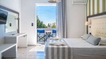 A modern hotel room with a bed, bedside table, and a desk with a chair. There is a balcony with a view of greenery and a clear sky.