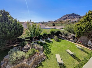 Un jardín bien cuidado con diversas plantas y árboles, un área de descanso con sillones, y una vista de un paisaje montañoso al fondo.