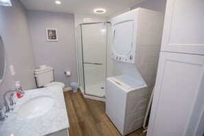 Une salle de bain équipée d’un lavabo, de toilettes, d’une douche à parois de verre et d’un lave-linge.