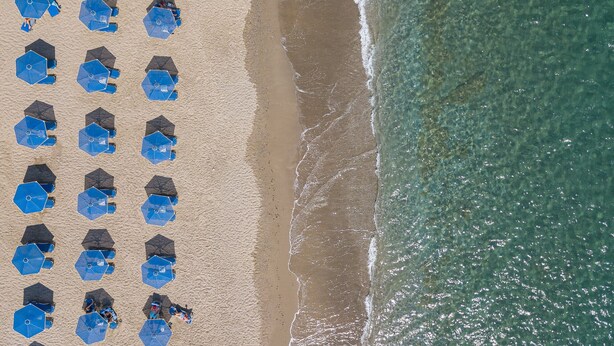 Vue aérienne d’une plage bordée de rangées de parasols bleus et de chaises de plage.