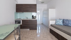 A compact kitchen with dark wooden cabinets, a glass-top dining table, and a built-in oven. - Mythos studio 5,near beach & tavern,South Crete (Damnoni)