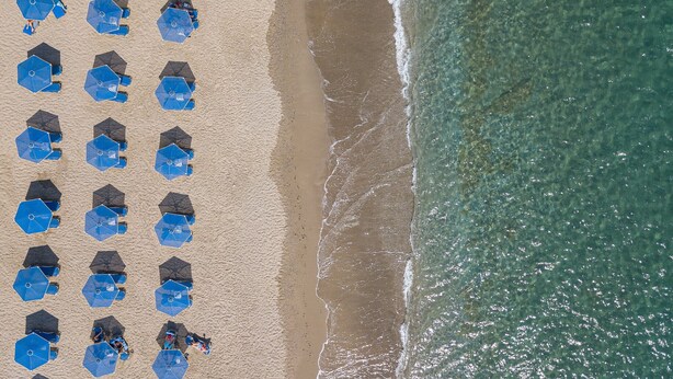 An aerial view of a beach with rows of blue umbrellas and beach chairs. - Mythos studio 5,near beach & tavern,South Crete (Damnoni)