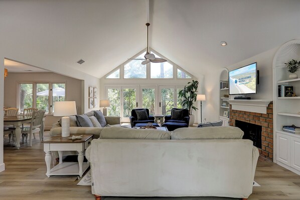 A spacious living room with a high ceiling, a fireplace, a television, and a dining area with a table and chairs.