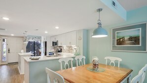 Una cocina moderna con armarios blancos, una mesa de comedor de madera y una lámpara colgante.