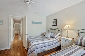 A bedroom with two beds, a nightstand with a lamp, a clock, and a door leading to another room.