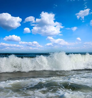 A beach with waves crashing onto the shore under a clear blue sky.