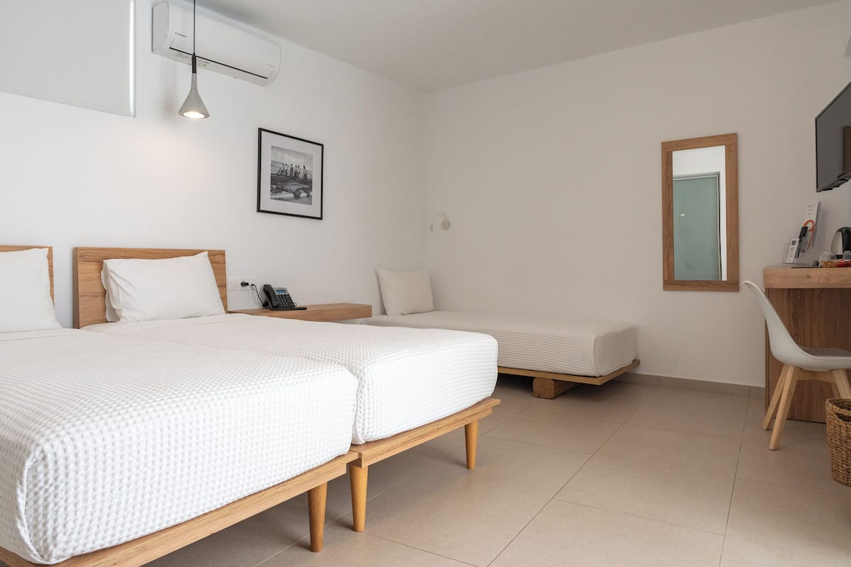 A hotel room with two beds, a desk, a chair, a bedside table, a lamp, a framed picture, and a mirror.