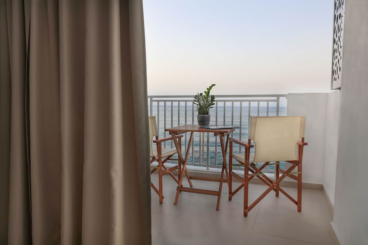 A balcony with a view of the sea, a small table with a plant, and two chairs.
