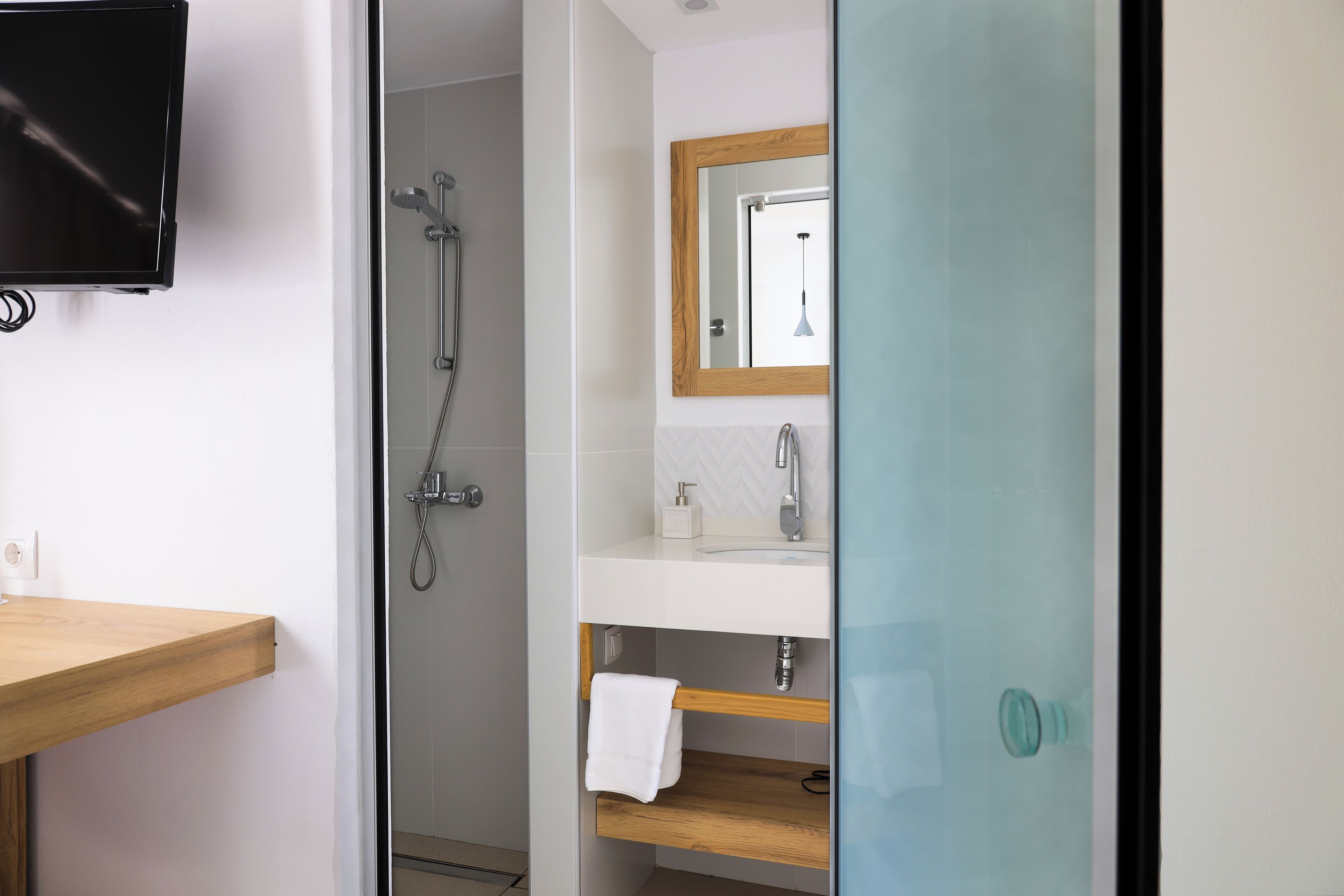 A bathroom with a wooden vanity, a mirror, a shower, and a television mounted on the wall.