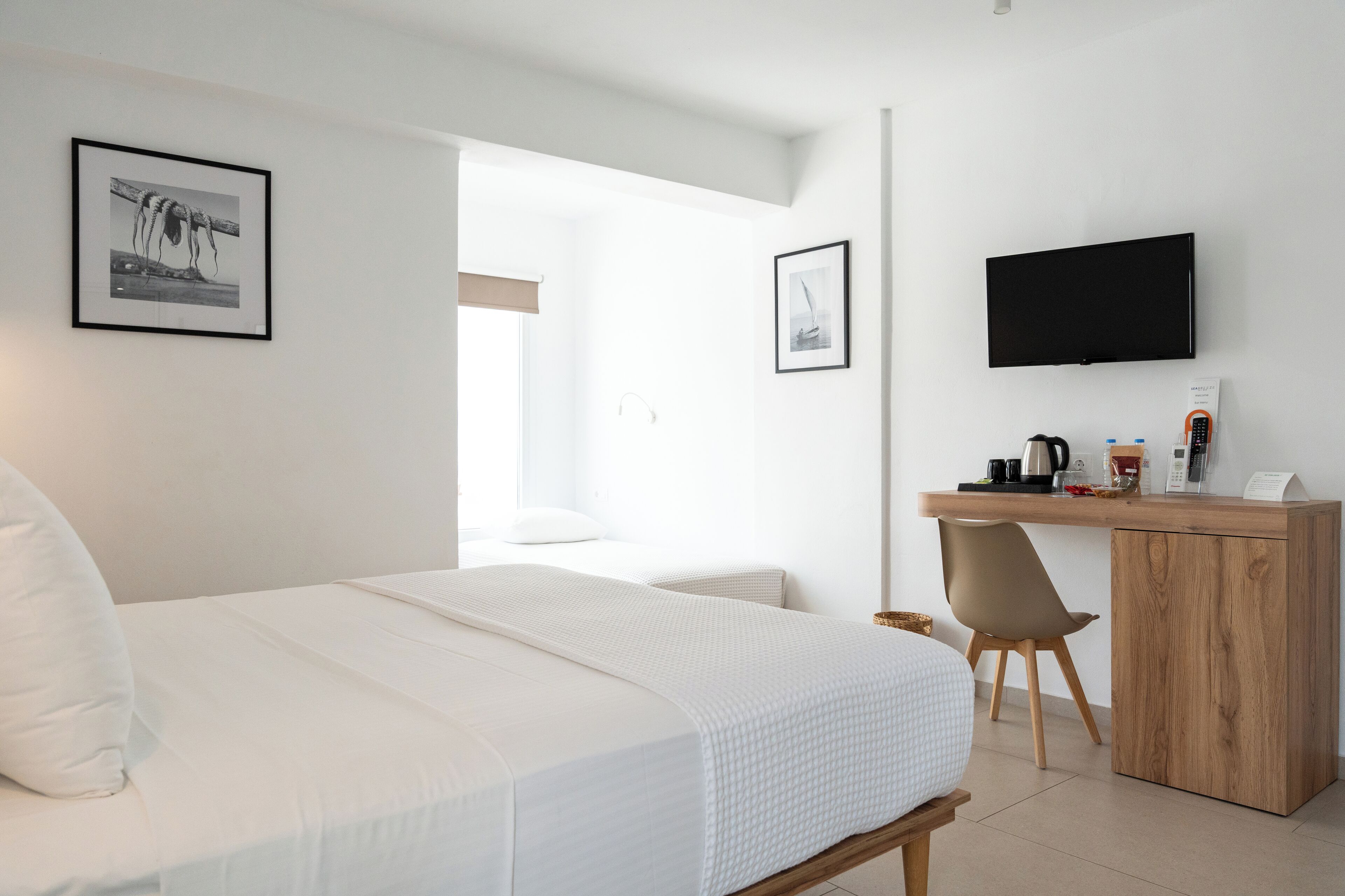 A modern hotel room with a bed, a desk, a chair, a television, and framed pictures on the walls.