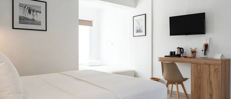 A modern hotel room with a bed, a desk, a chair, a television, and framed pictures on the walls.
