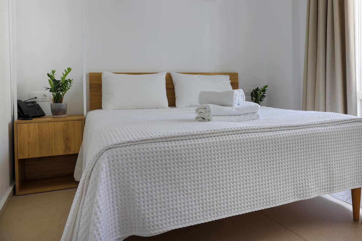 A neatly made bed with white bedding, a wooden headboard, and two bedside lamps.