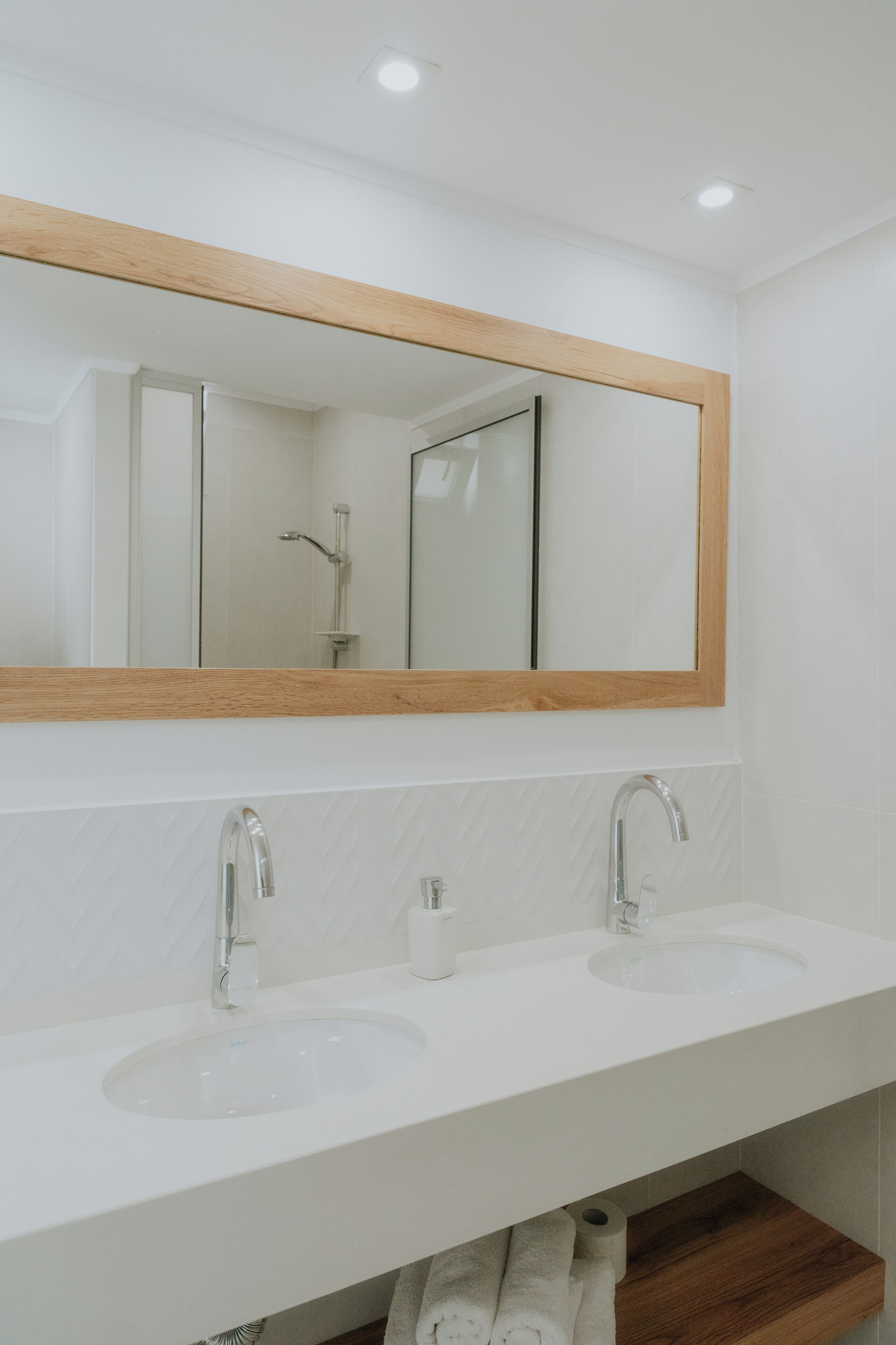 A modern bathroom with a wooden-framed mirror above a white sink and vanity.