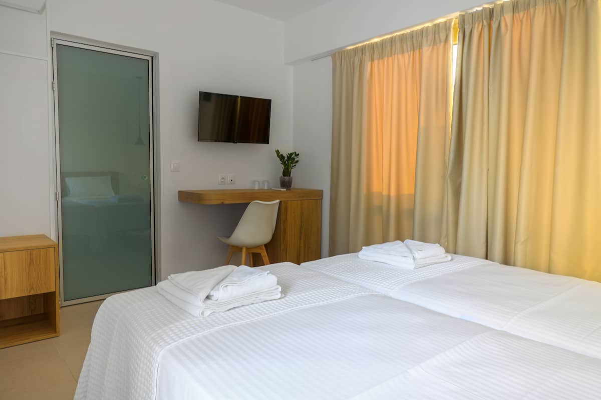 A hotel room with a bed, a desk, a chair, a TV, and a sliding door.