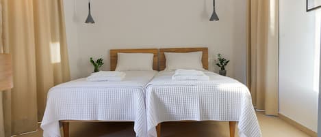 Un lit double avec une literie blanche, deux tables de chevet, une petite plante en pot et un luminaire suspendu.