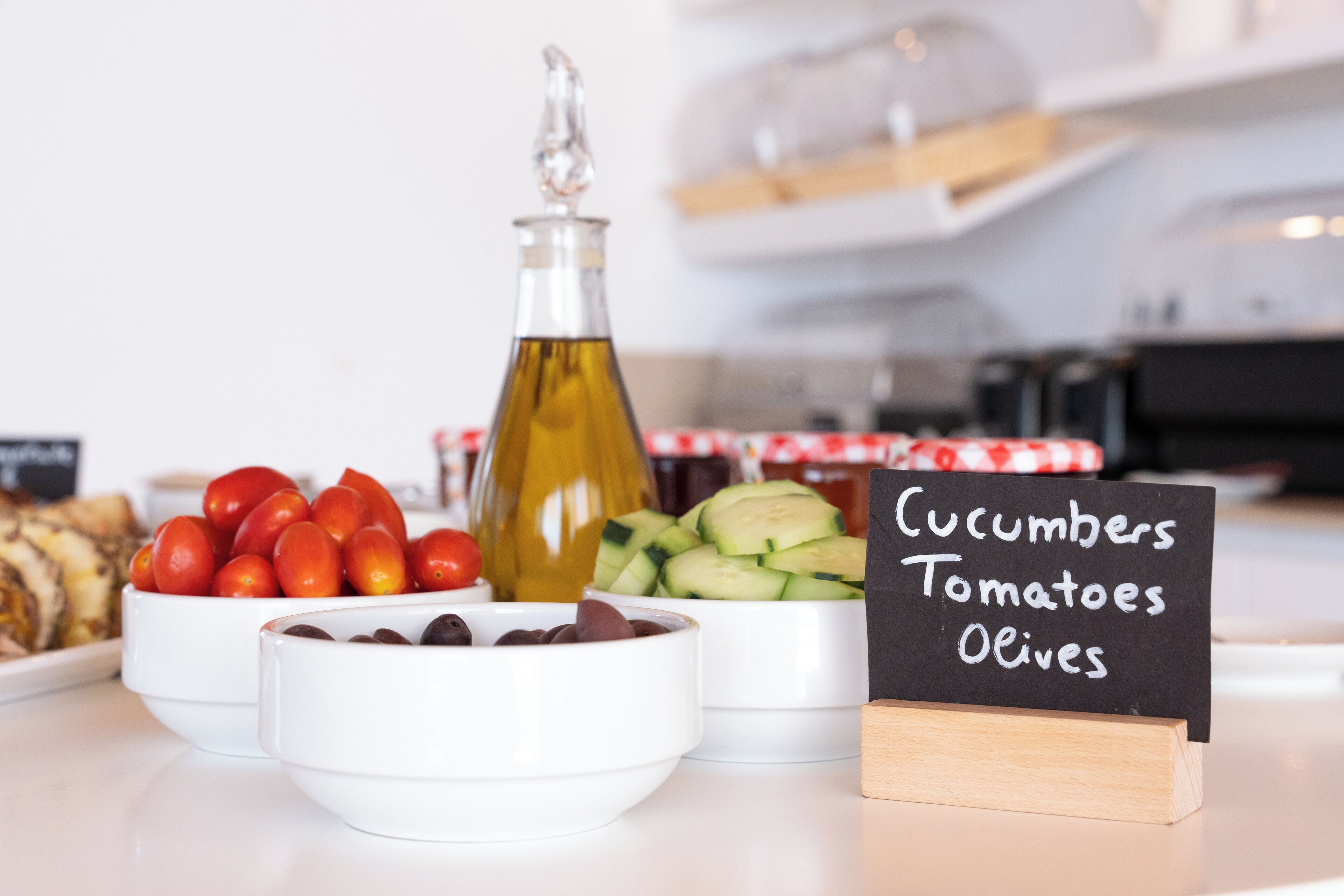 A table with bowls of cucumbers, tomatoes, and olives, and a bottle of olive oil.