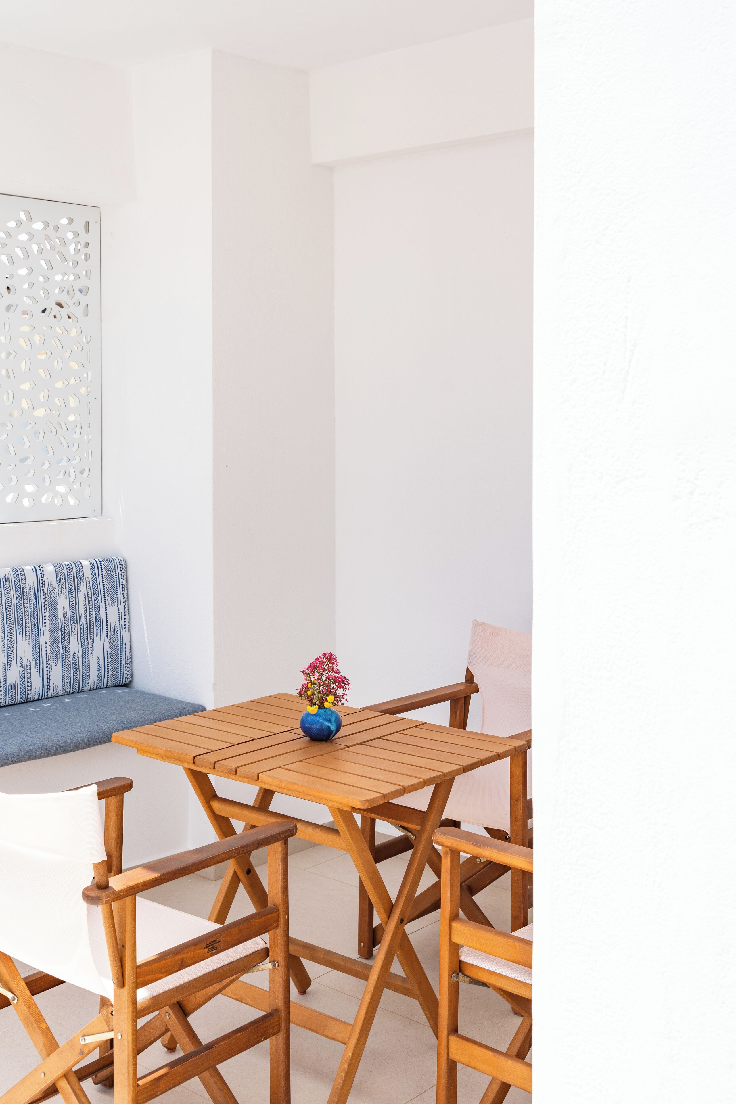 A wooden table and chairs set in a room with a white wall and a patterned cushion.