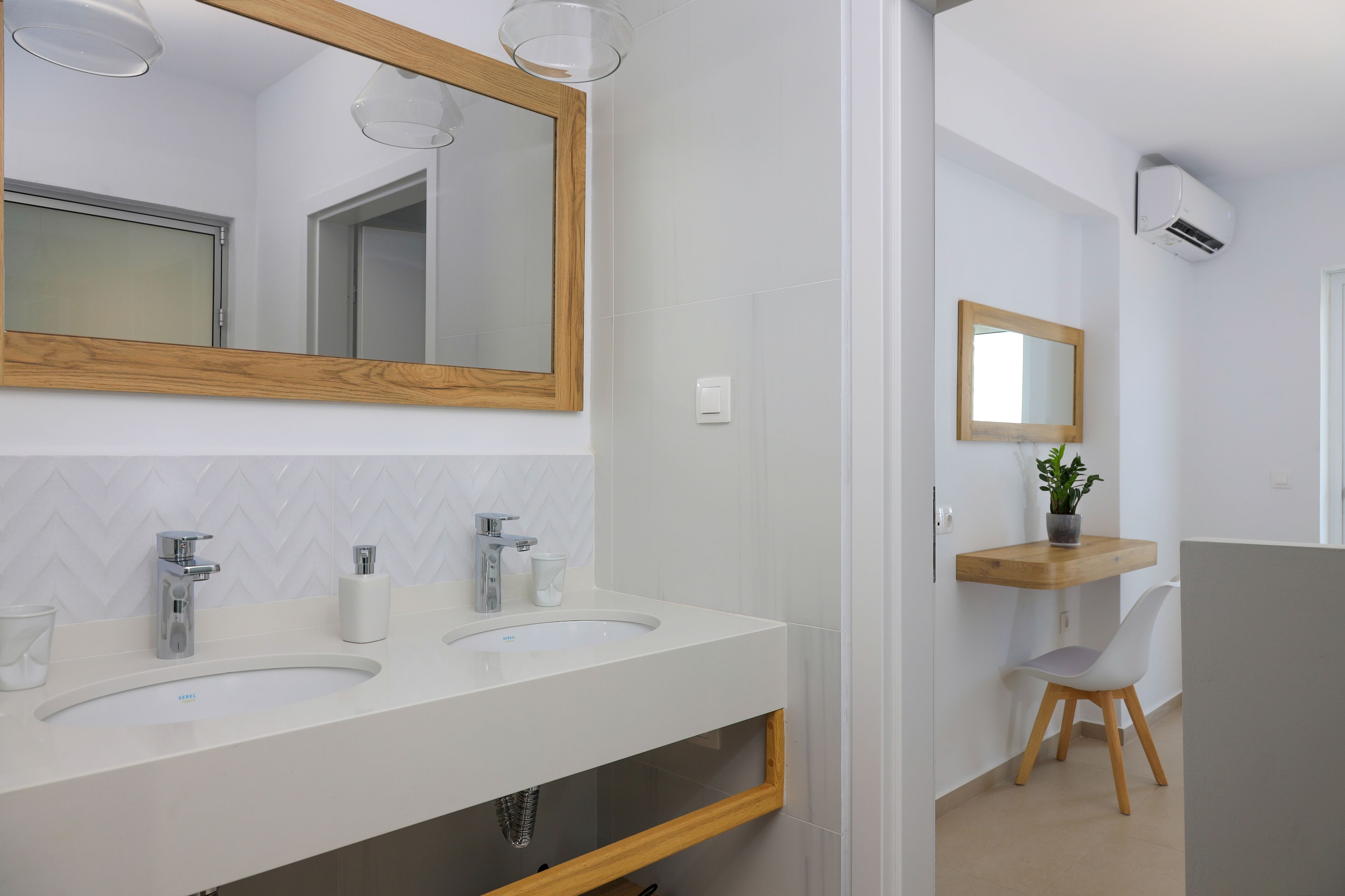 A modern bathroom with two sinks, a large mirror, and a wooden shelf with a plant.