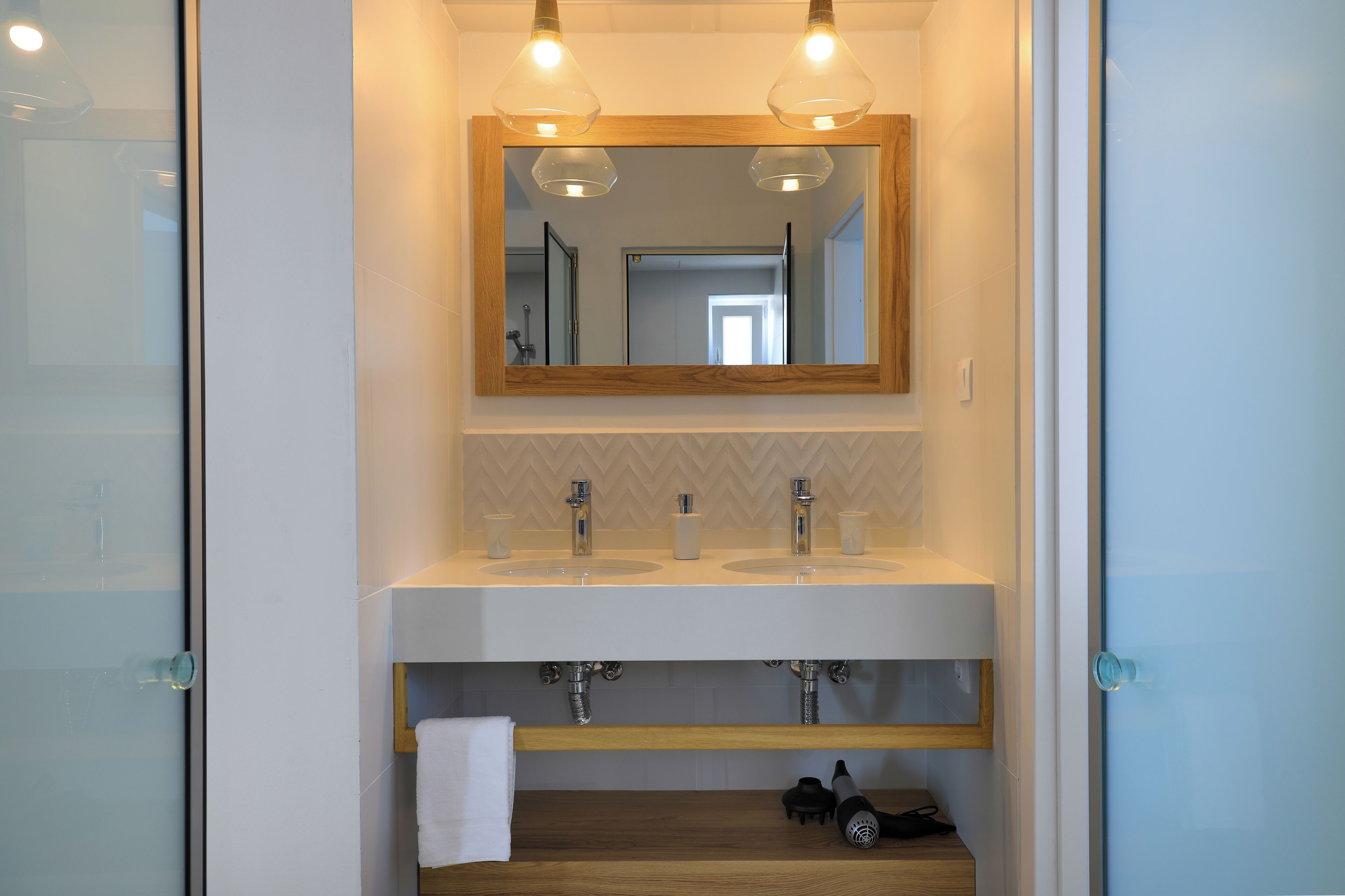 Une salle de bain moderne avec deux vasques, un miroir et des luminaires suspendus.