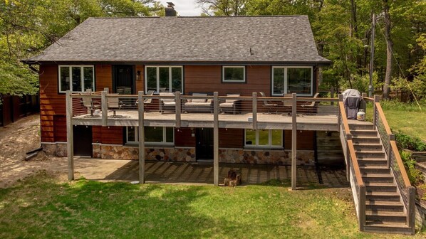 A two-story house with a deck, stone foundation, and a wooden staircase. - Protected Channel, Swimming, Fishing from Dock (Crosslake)