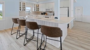 Een moderne keuken met een centraal eiland, barstoelen, witte kasten en uitzicht naar buiten.