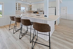A modern kitchen with a central island, bar stools, white cabinetry, and a view to the outside.