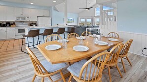 Een moderne keuken met witte kasten, een houten eettafel gedekt voor zes personen, en uitzicht op de oceaan door grote ramen.