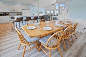 A modern kitchen with white cabinets, a wooden dining table set for six, and a view of the ocean through large windows.