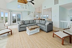 A spacious living room with a large gray sectional sofa, a wooden coffee table, and a view of the outdoor balcony.