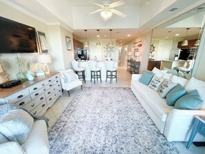 A spacious living room with a large white sofa, a dining area with a central island, and a kitchen in the background. - Stunning 1/1 marina condo just miles from beaches (Orange Beach)