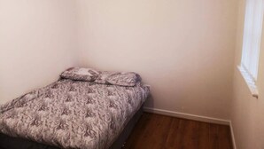 A small, single-bed room with a patterned bedspread, a ceiling fan, and a window with a white blind.